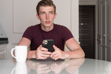 Young man drinks coffee and uses a mobile phone