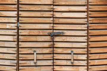 Wooden door with an accordion on hinges. The door leaves are folding in two directions. Closed with a metal padlock. Concept of a small warehouse for tools, inventory.
