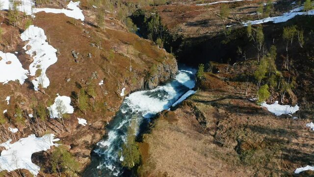 Aerial view overlooking a waterfall in snowy nature, sunny, summer day, in the Lyngen alps, North Norway - Pull back, drone shot