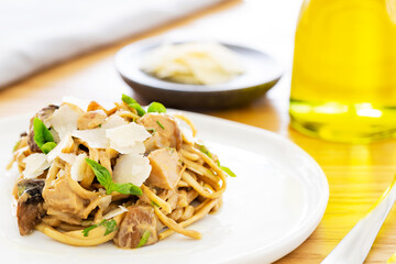Close-up on some porcini mushroom cream sauce linguini pasta with basil and parmesan. With a bottle of olive oil, a grey napkin and parmesan on the side. White plate on an oak table.