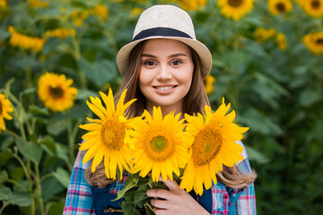 Young, adorable, female farmer holding many beautiful sunflowers in the middle of a green and golden sunflower field.