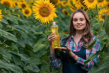 Gorgeous, young, adorable, female farmer holding a bottle of sunflower oil in the middle of a...