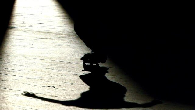 Skateboarder does a trick on a fully backlit silhouette image within a beam light that cuts the image vertically. Nollie bs heelflip the name of the trick