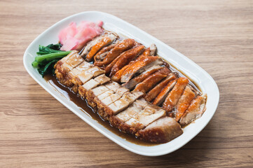 Juicy crispy pork and roasted duck in a white dish on a wooden table.