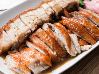 Juicy crispy pork and roasted duck in a white dish on a wooden table. Close up