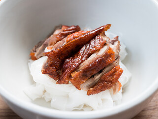 Wide rice noodle topped with roasted duck served in a white bowl, without soup