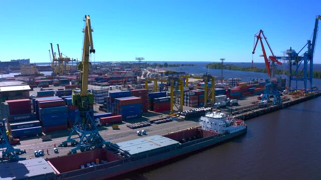 Aerial view of a row of construction or cargo cranes on the river bank with a barge standing nearby. Ship docks off Kanonersky Island. Industrial port with water barges and transport tugs.