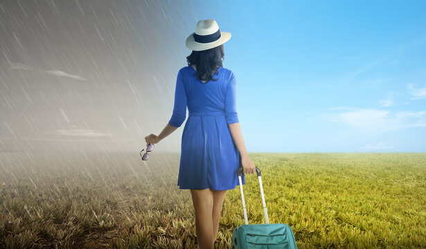 Asian woman with suitcase standing on the meadow field with a different climate
