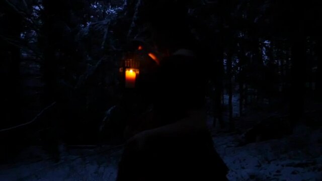 Woman holding lantern walking in the forest in the winter at Dawn. Wearing a ball dress.