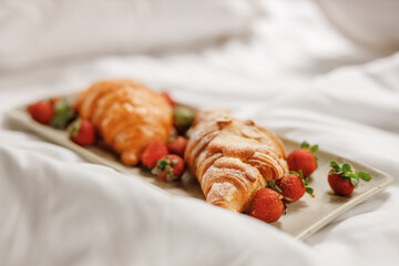 Breakfast in bed, tray with  croissant on white sheets