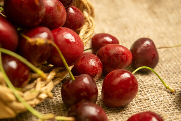 Ripe juicy cherries in a wicker basket and cherries scattered on a homespun fabric with a rough texture. Close up.