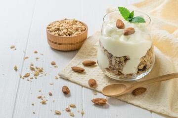 A small wooden spoon next to a glass of yogurt and granola.