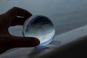 Hand is holding glass sphere on water and city reflected in,close up.