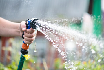 Gardener is watering a garden bed by a water sprinkler close up.