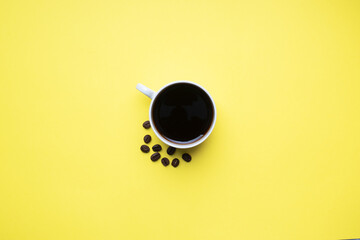 Black coffee in a Cup and coffee beans on a yellow background. Top view Copy space.