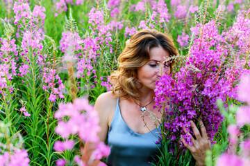 Beautiful woman in gray dress relaxes with bunch of flowers on fireweed meadow