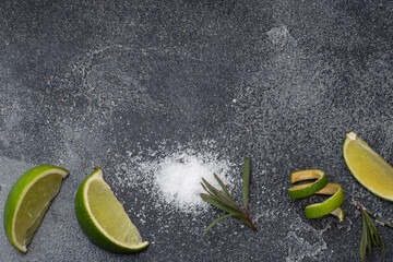 Slices of fresh lime, salt and rosemary dark concrete background. Copy space. Ingredients for...