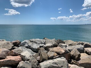 Background texture: large stones of various shapes in the sea. A pile of granite boulders against the background of the sea and sky. Rock destroyed by the waves. Concept - stone, hardness