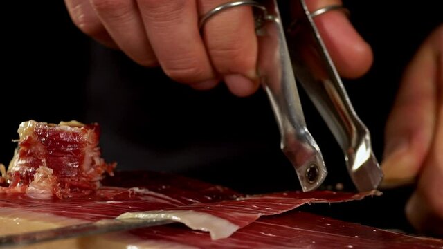Ham cutter master gets  a slice of Iberico ham with his tongs,  in a short image detail. Very appetizing to eat that delicacy, with impressive red and white colors