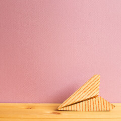 Stripe pattern paper plane on wooden table with pink copy space