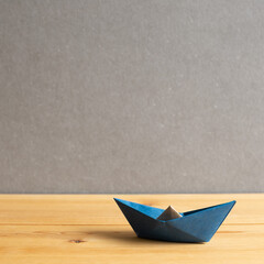 Blue paper ship on wooden table with gray copy space