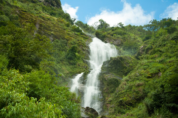 Scenic landscape of cascade Thac Bac Waterfall (Silver Falls) in mountains with lush green trees and blue sky, Northern Vietnam, Sapa town