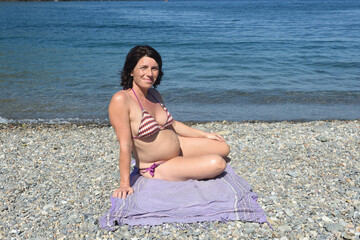 Fototapeta na wymiar pregnant woman sitting and sunbathing on the beach,looking at camera