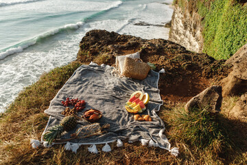 Beautiful summer picnic on the beach at sunset in boho style. Picnic background with basket, baguettes  and fruits by the ocean..