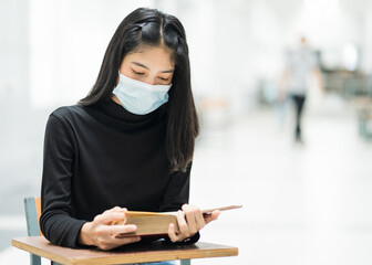 Portrait of a teenager college student wears face mask while reading book in college campus to prevent COVID-19 pandemic.