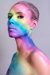 Portrait of a young woman with rainbow makeup posing in the studio. Creative body art with colored overflows on female head and shoulders.