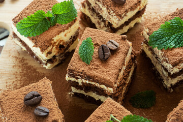 Pieces of tiramisu cake with delicate cream, coffee beans and mint leaves.