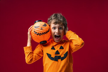 Happy Halloween! Cute boy with pumpkins scares on red background. traditionally