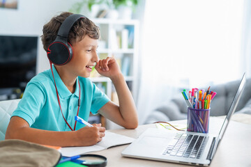 cheerful boy with headphones uses laptop to make a video call with his teacher.