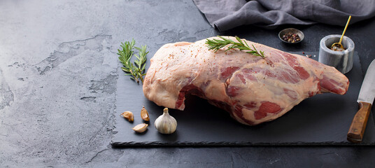 Raw lamb leg with spices and herbs on marble cutting board. Dark background. Copy space.