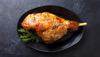 Roasted lamb leg on a plate. Black background. Close up. Top view.