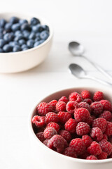 Raspberries and blueberries close-up in bowls on a white background, ripe juicy berries