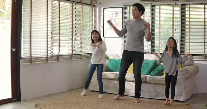 Happy family dancing in living room. Young adult asian parents dad and cute little daughter listening music and dance together having fun enjoying leisure lifestyle at home. Stay at home quarantine.