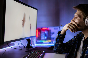 young male person sitting in front of the screen and watching the horror movie at night, scary emotions