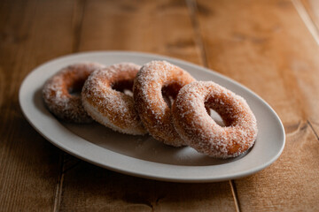 delicious sugar doughnuts on a white plate on a wooden board. the photo is very simple but looks very yummy. sugar doughnuts are easy to make and also perfcet for a snack or sugary breakfast.