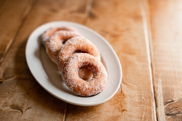delicious sugar doughnuts on a white plate on a wooden board. the photo is very simple but looks very yummy. sugar doughnuts are easy to make and also perfcet for a snack or sugary breakfast.
