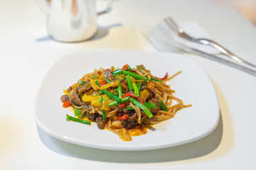 Asian noodles with different vegetables and meat in a white plate on the table close-up