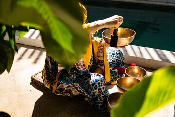 attractive young pregnant woman in colored atlas kimono dress with a singing bowl sitting and playing on summer terrace 