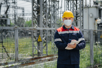 An electrical substation engineer inspects modern high-voltage equipment in a mask at the time of pondemia. Energy. Industry