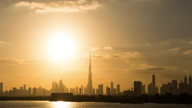 A magnificent time-lapse from day to night of Dubai skyline with the majestic sunset on the background as the beautiful clouds pass by on the world tallest building, an extremely long and static shot.