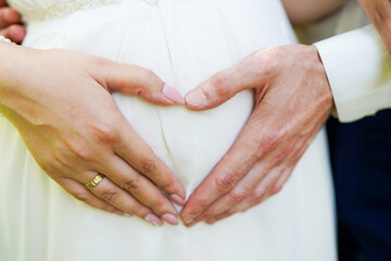 Groom and bride making a heart sign while their arms are on her stomach