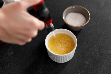 cooking, food and culinary concept - close up of hand with burner burning sugar crust in baking dish