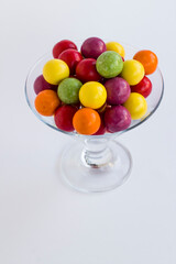 Colorful candies in transparent glass bowl on grey background.