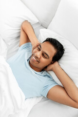 people, bedtime and rest concept - happy smiling indian man lying in bed at home