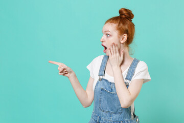Fototapeta premium Shocked young readhead girl in casual denim clothes posing isolated on blue turquoise background studio. People lifestyle concept. Mock up copy space. Pointing index finger aside, put hand on cheek.