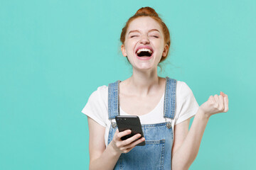 Joyful young readhead girl in casual denim clothes posing isolated on blue turquoise background...